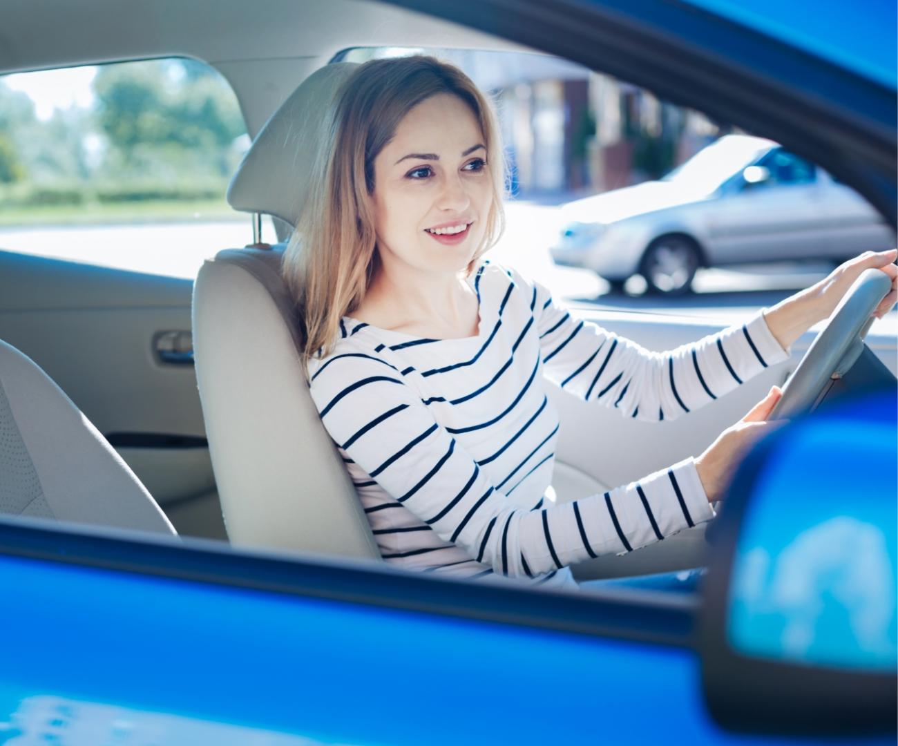 Smiling woman driving a blue car.