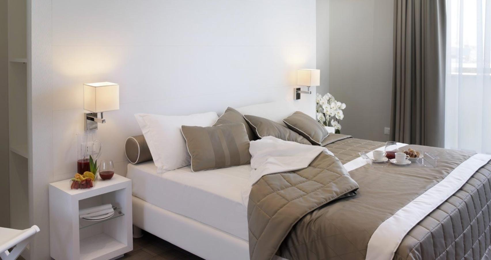 Camera da letto moderna con letto matrimoniale, cuscini grigi e colazione sul letto.