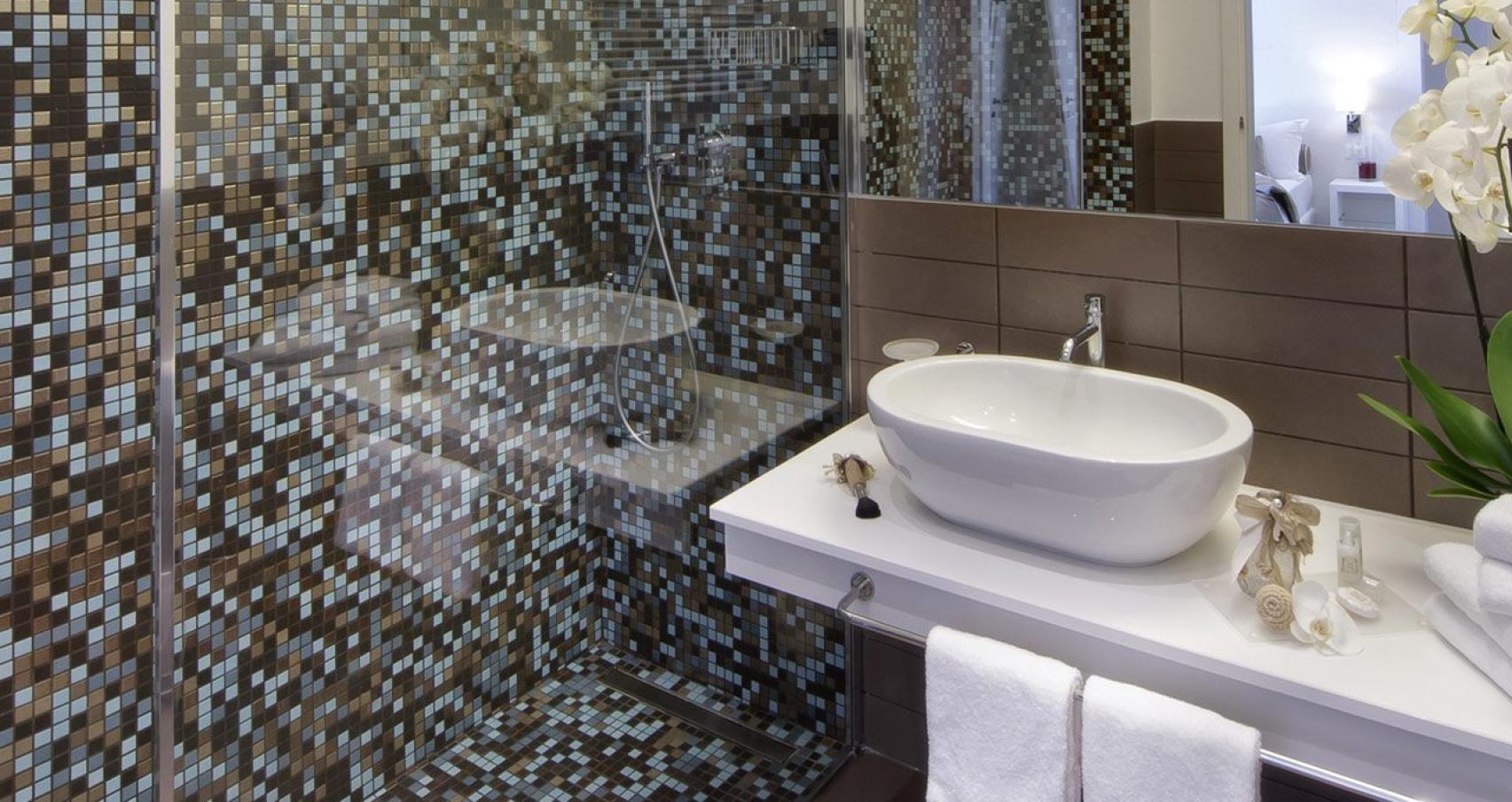 Bagno moderno con doccia a mosaico, lavabo bianco e asciugamani bianchi.