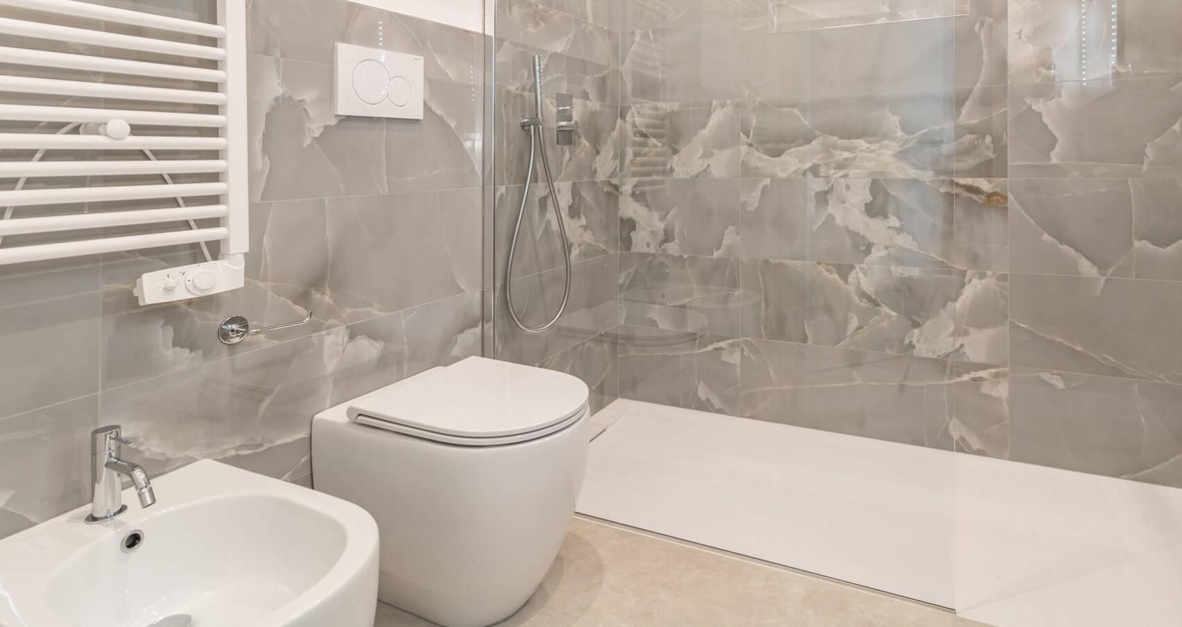 Bagno moderno con doccia a pioggia e sanitari bianchi su piastrelle effetto marmo.