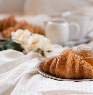 Breakfast with croissants, honey, and white flowers on a bed.