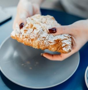 Person holding a powdered sugar-dusted croissant over a gray plate.