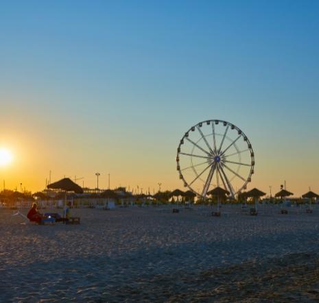 Spiaggia al tramonto con ruota panoramica e ombrelloni.