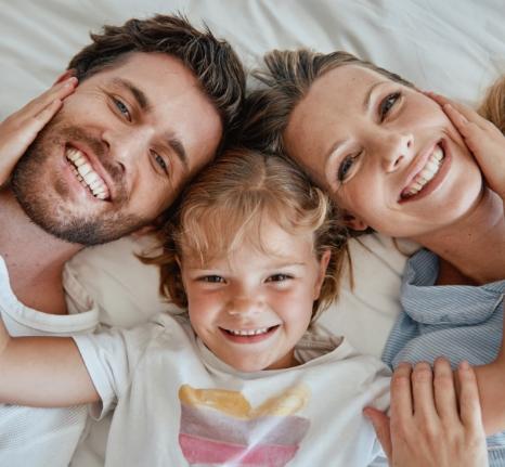 Famiglia felice sorridente distesa su un letto, genitori e figlia insieme.